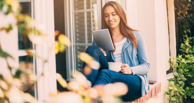 Femme à l'aide d'une tablette tout en tenant une tasse de café