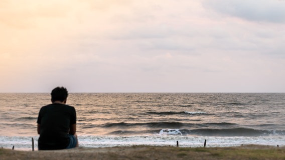 A person sits alone by the sea, slightly slumped.  © Imago Images / Panthermedia Photo: Panthermedia