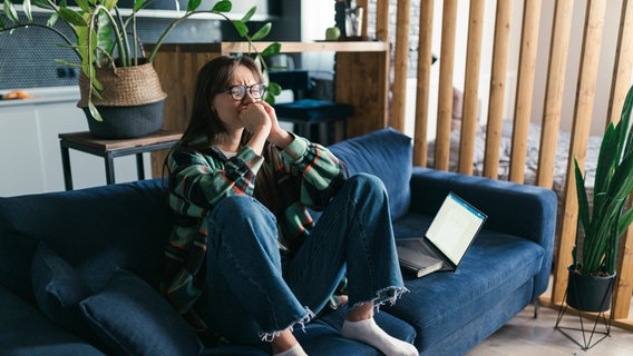 A desperate young woman sits on a sofa next to a laptop and a book.  © imago images Photo: Westend61