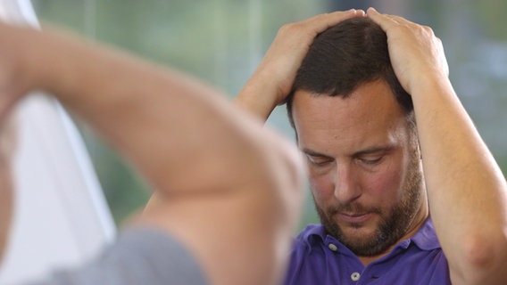 Movement doctor Christian Sturm places his clasped hands on the back of his head and lets his chin sink. © NDR Photo: Moritz Schwarz/Oliver Zydek