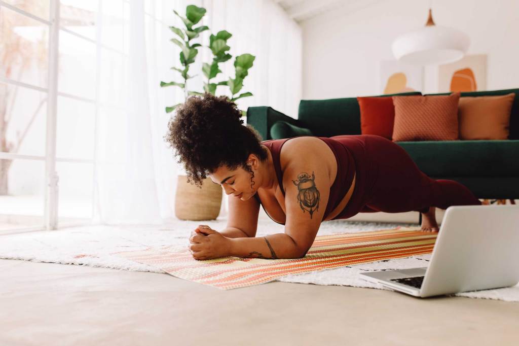 Woman doing plank workout with laptop at home