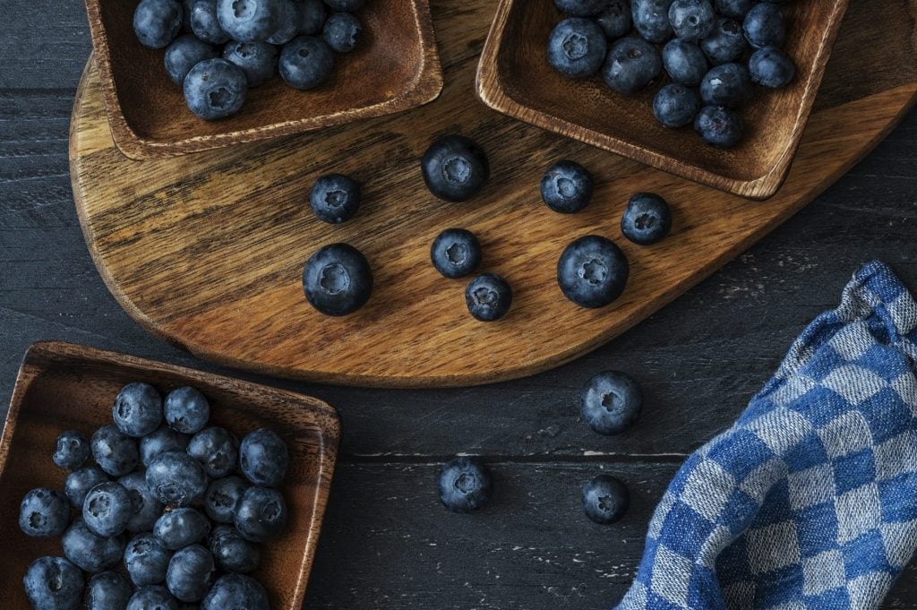 High-fiber foods: wooden bowls with blueberries on a dark wooden table