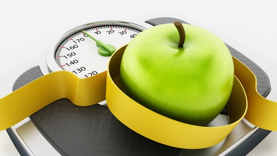 A green apple with a measuring tape lies on a scale. © picture alliance Photo: Cigdem Simsek