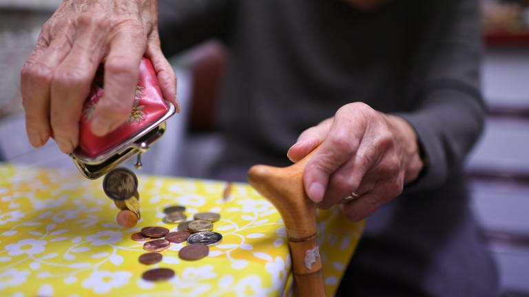 A pensioner pours change from a purse onto the kitchen table.