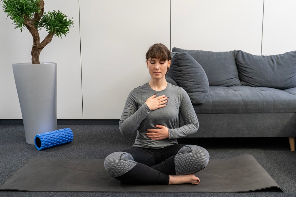 A woman meditates cross-legged on the floor.