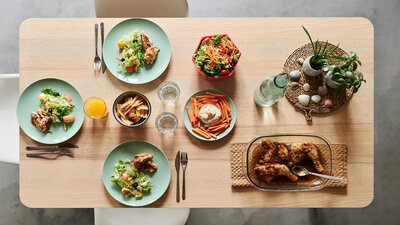 Three plates are set on a table with salad and chicken arranged on them.