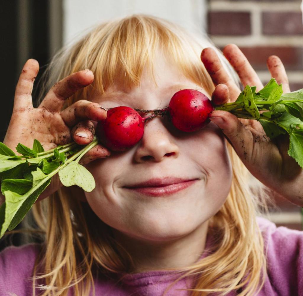 Smiling girl holding covering eyes with fresh radish on balcony