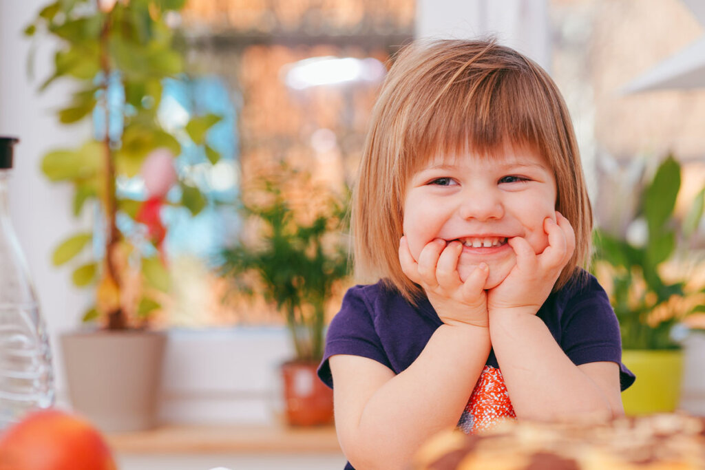 A small child stands in front of a kitchen counter and smiles.