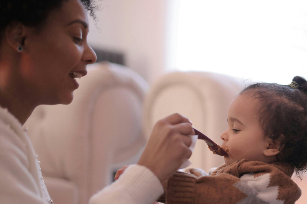 A woman gives her baby porridge with a spoon.