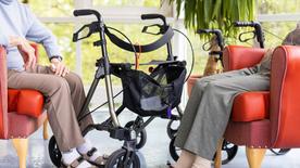 Two residents of a nursing home sit next to their walkers.