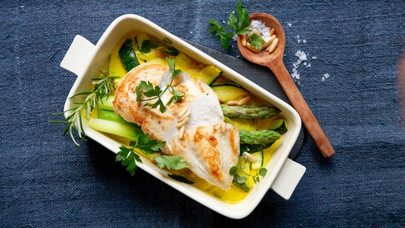 A casserole dish with asparagus and zucchini casserole with chicken fillet is on a table. © NDR Photo: Claudia Timmann